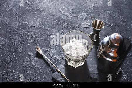 Bar utensili per la realizzazione di cocktail. Shaker e un bicchiere di ghiaccio sulla pietra scura tabella. Spazio di copia Foto Stock
