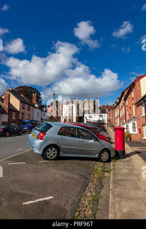 Auto parcheggiate su abbassare Broad Street Ludlow, rovina la vista delle case storiche e town gate su per la collina verso il centro città, Shropshire, Regno Unito Foto Stock