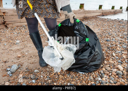 Una donna che utilizza un selettore di figliata mette i rifiuti plastici trovati sulla spiaggia in un nero sacco della spazzatura durante una comunità spiaggia pulita. Foto Stock