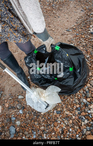 Una donna che utilizza un selettore di figliata mette i rifiuti plastici trovati sulla spiaggia in un nero sacco della spazzatura durante una comunità spiaggia pulita. Foto Stock