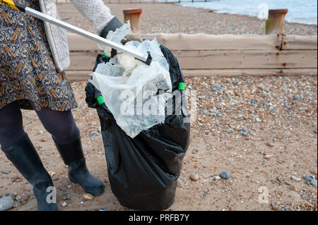 Una donna che utilizza un selettore di figliata mette i rifiuti plastici trovati sulla spiaggia in un nero sacco della spazzatura durante una comunità spiaggia pulita. Foto Stock