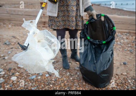 Una donna che preleva i rifiuti in plastica utilizzando un selettore di lettiera dalla spiaggia durante una comunità spiaggia pulita. Foto Stock