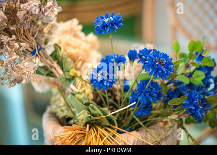 Secchi fiori blu e di frumento, sedie di vimini in sala da pranzo con grande tavolo in vetro e decorazioni. Accogliente, vintage, rustica atmosfera in casa. Concetto di Foto Stock