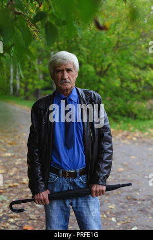 Grigio-uomo dai capelli con un ombrello nelle sue mani sulla strada. Un uomo è di 60 anni. Foto Stock