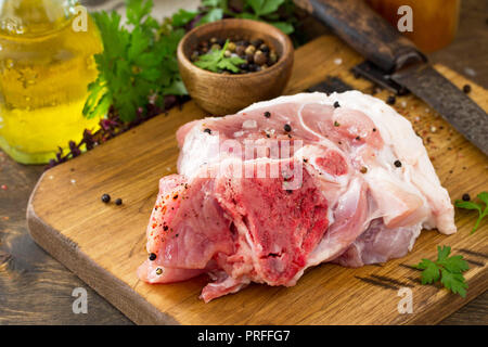 Fresco la carne cruda. Carne di maiale cruda bistecca con l'olio d'oliva, erbe e spezie su un tavolo di legno. Foto Stock