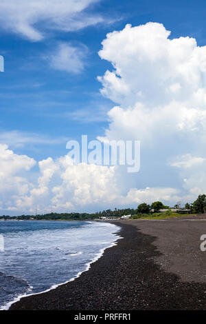 Ocean Beach con sabbia nera vulcanica contro nuvoloso cielo blu. Paesaggio estivo spiaggia nera di Bali, Indonesia Foto Stock