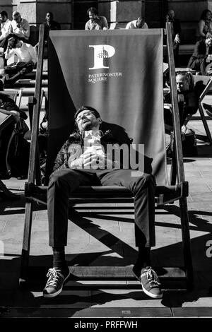 Un giovane uomo addormentato in una grande sedia a sdraio durante una pausa pranzo, Paternoster square, London, Regno Unito Foto Stock