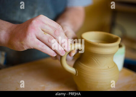 Professional potter maschio lavora in officina, studio - mettere la maniglia sul vaso di ceramica. Fatti a mano, small business, creazione di concetto di lavoro Foto Stock