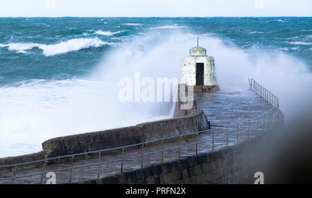 Mare mosso e le onde si infrangono e rottura sulle pareti del porto e poco bianco torretta casa stile sull'estremità Foto Stock