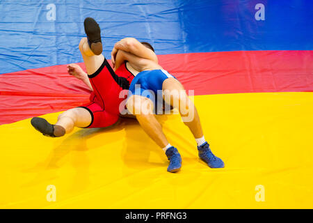 Due giovani uomini in blu e in rosso il wrestling su un giallo tappeto di wrestling in palestra Foto Stock