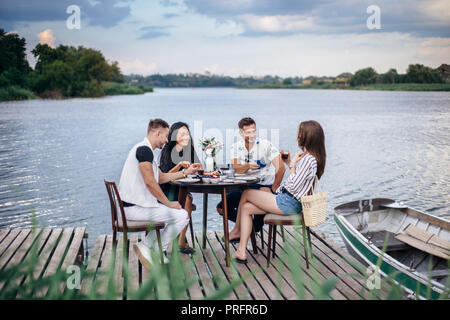 Il gruppo di amici di felice incontro a cena insieme a picnic estivo. Cibo, mangiare e il concetto di divertimento Foto Stock