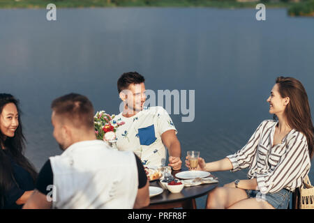 Amici divertendosi durante la cena nel ristorante all'aperto. Cibo, divertimento e concetto di pranzo Foto Stock