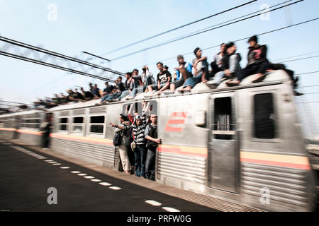 Giovani uomini che cavalcano in cima alla folla Mass Rapid Transit treno a Giacarta, Java, Indonesia Foto Stock