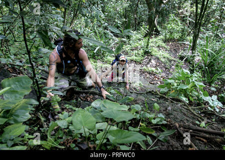 Giovani uomini che arrampicano su roccia faccia coperta di vegetazione nel Parco Nazionale di Taman Wisata Alam Pangandaran, Giava, Indonesia Foto Stock