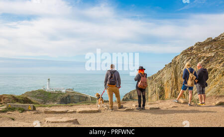 Vista posteriore del popolo stava in piedi al sole (A RSPB Sud pila scogliere) fissando il paesaggio: guardando fuori in mare a sud del faro di stack, Anglesey, Regno Unito. Foto Stock