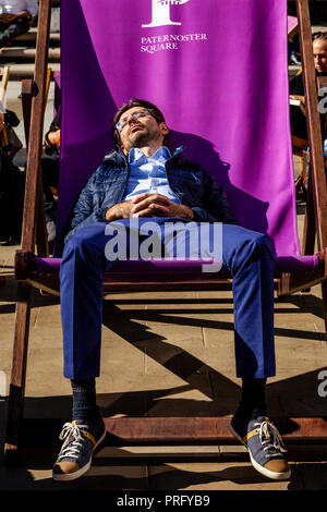 Un giovane uomo addormentato in una grande sedia a sdraio durante una pausa pranzo, Paternoster square, London, Regno Unito Foto Stock