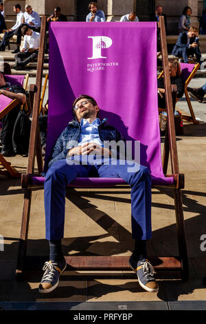 Un giovane uomo addormentato in una grande sedia a sdraio durante una pausa pranzo, Paternoster square, London, Regno Unito Foto Stock