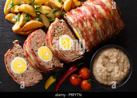 Hackbraten pagnotta di carne con uovo servite con spicchi di patate e salsa di close-up su una piastra di ardesia sul tavolo. parte superiore orizzontale vista da sopra Foto Stock