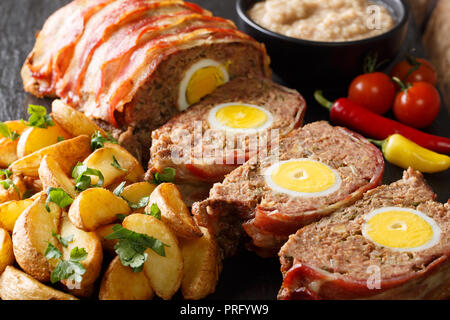 Spicy tedesco pagnotta di carne avvolti in pancetta con spicchi di patate e salsa di close-up su uno sfondo nero. orizzontale Foto Stock