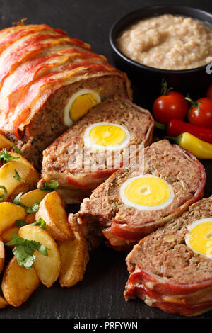 Hackbraten pagnotta di carne con uovo servite con spicchi di patate e salsa di close-up su una piastra di ardesia sul piano verticale. Foto Stock