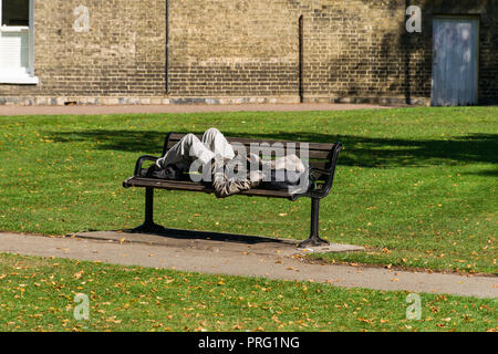 Un giovane uomo trova appoggio o addormentati al sole su una panchina nel parco, Cristo pezzi unici, Cambridge, Regno Unito Foto Stock