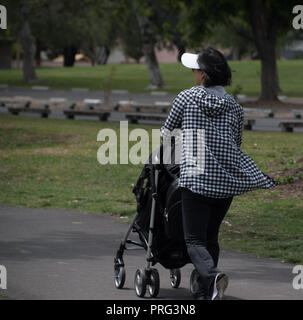 Una donna con una passeggiata in Yorba Parco Regionale in Yorba Linda, CA con il suo bambino in un bambino nero carrello con tavoli da picnic in background in 2018 Foto Stock