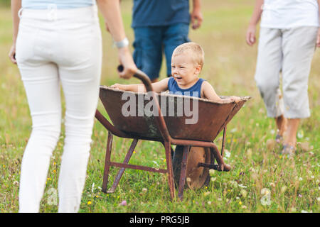 Famiglia spingendo il loro bambino piccolo e nipote in una carriola Foto Stock