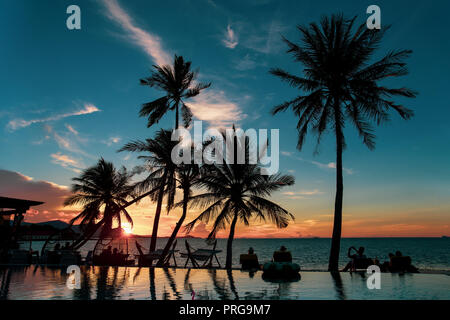 Silhouette Palm tree e il gruppo di turista guardando il tramonto sul mare. Foto Stock