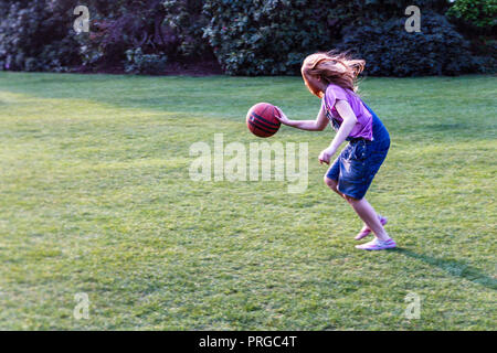 Colpo di movimento di una ragazza di 10 anni dribbling di un basket di tutta l'erba nel parco Foto Stock