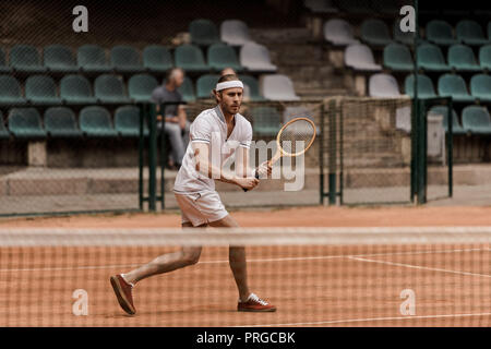 Concentrato in stile retrò uomo giocando a tennis a corte Foto Stock