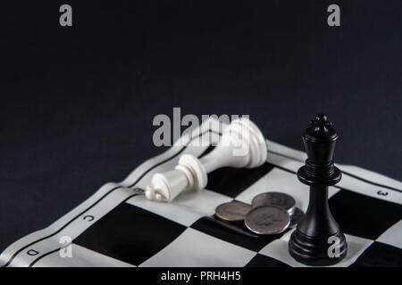Due re di scacchi in piedi di fronte ad ogni altro, monete tra di loro. Re bianco caduti. Strategia, finanza, business concetto. Foto Stock