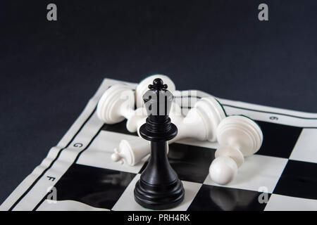 Scacchi nero re permanente sulla scacchiera, re bianco caduto con pedine. Strategia, finanza, business concetto. Foto Stock