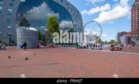Vista al di fuori del mercato hall di Rotterdam con una grande ruota panoramica Ferris e gruppi di persone e ciclisti sulla piazza di fronte al palazzo Foto Stock