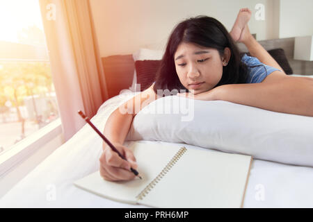 Girl Teen rilassarsi facendo i compiti a casa sul letto in camera da letto al mattino tutti i giorni Foto Stock
