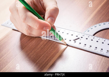 Carpenter utilizzando un goniometro ed effettuare un contrassegno in corrispondenza del punto di misurazione con una matita su una tavola di legno Foto Stock