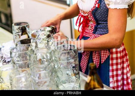 Bella ragazza in un grembiule azienda tazze il loro riempimento con sfondo di birra Oktoberfest bicchieri. Foto Stock