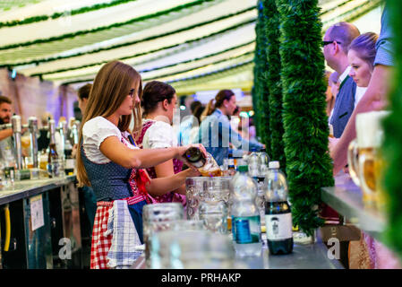 Koblenz Germania -26.09.2018 bella ragazza in un grembiule azienda tazze il loro riempimento con sfondo di birra Oktoberfest bicchieri. Foto Stock