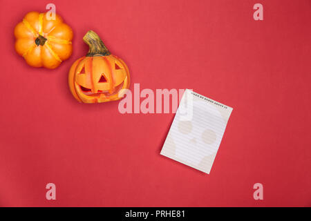 Halloween zucca scolpita divertenti e viso carino lungo con piena intatto zucca lungo le note carta su sfondo rosso Foto Stock