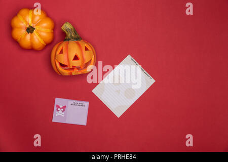 Halloween zucca scolpita divertenti e viso carino lungo con piena intatto zucca lungo due note su carta su sfondo rosso. Foto Stock