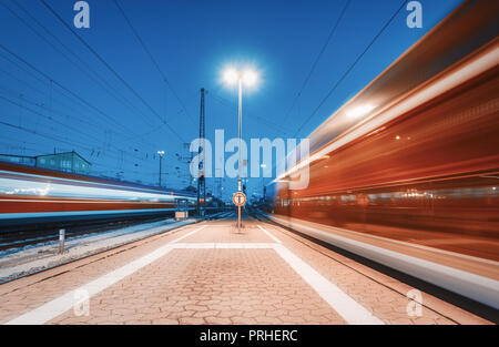 Due treni ad alta velocità in movimento sulla stazione ferroviaria di notte. Sfocata in movimento moderno treno intercity sulla piattaforma ferroviaria in Europa. Ra passeggero Foto Stock