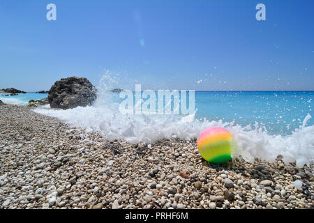 Sfera colorata su di una spiaggia di ciottoli, spruzzata con onde e schiuma di mare Foto Stock