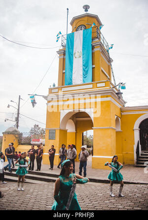 Marching Band ballerini sfilano in processione sotto una bandiera Guatemalteca in Ciudad Vieja, una piccola città al di fuori di Antigua Foto Stock