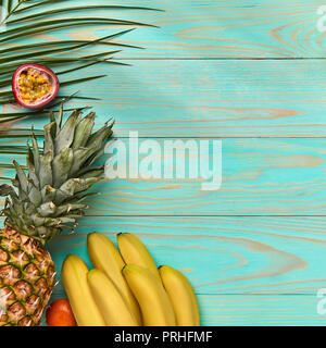 Interi pezzi di succosa frutta esotica e Verde foglie di palmo su un blu sullo sfondo di legno con spazio per il testo. Telaio di cibo. Lay piatto Foto Stock