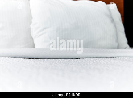 Bianco ripiegato il copriletto e i cuscini su un letto fatto con profondità di campo Foto Stock