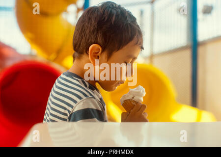 Ragazzo di mangiare una pallina di gelato nel parco giochi Foto Stock