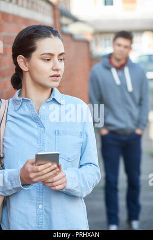 Giovane donna Texting per aiutare sul telefono cellulare pur essendo sgambate su strada di città Foto Stock