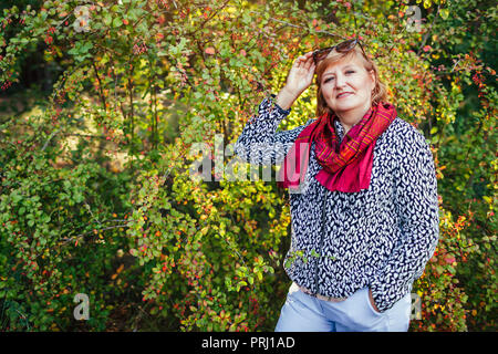 Elegante donna di mezza età in posa nella foresta di autunno. Senior lady caduta da indossare capi di abbigliamento e accessori. La moda Foto Stock