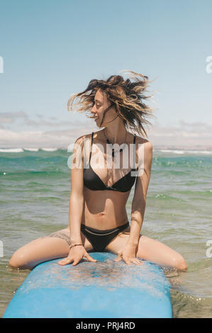 Giovane donna in bikini seduta sul bordo di surf in ocean Foto Stock