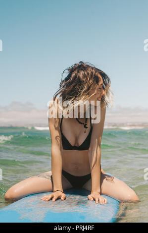 Giovane donna allegra in bikini seduta sul bordo di surf in ocean Foto Stock