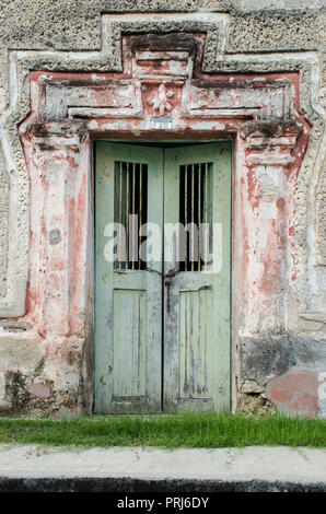 Il Blue Door incorniciata su un telaio di rosa, su un vecchio muro rotto circondato dai polverosi e rusty pietre, sul bordo del marciapiede di una strada. Foto Stock